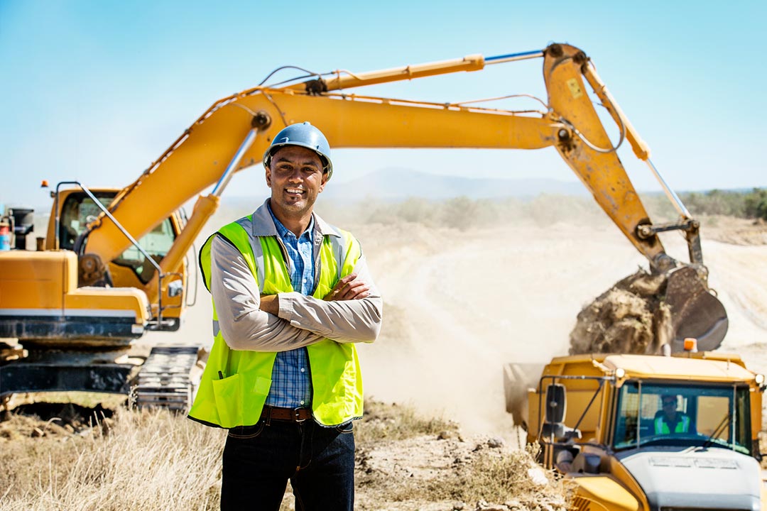 A male contractor standing in front of a project they are breaking ground on with a tractor in the background